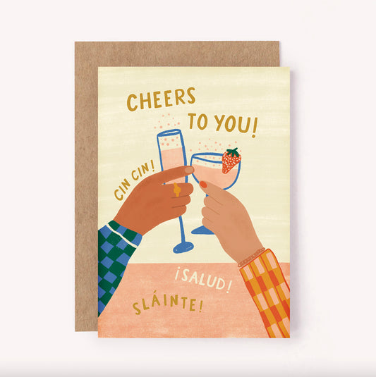 Illustrated "Cheers to You!" birthday card with two hands holding clinking glasses of champagne and a cocktail. Soft palette of beige, pink and gold with bold patterened sleeves.