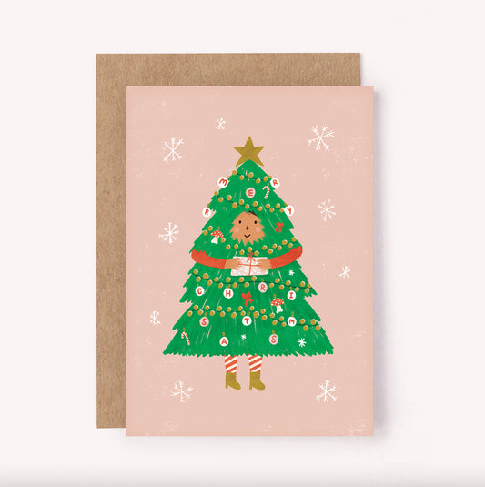Cute illustrated Christmas card. Pink background with a girl dressed as an Xmas tree, decorated with mushroos, ribbons, candy canes and baubles
