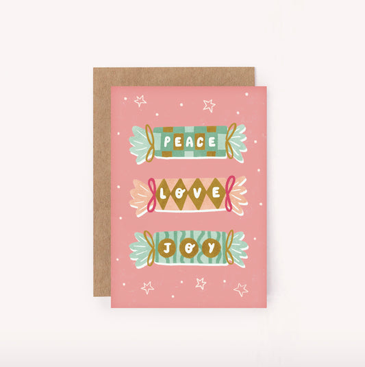 Send some Peace, Love & Joy with this illustrated mini Christmas card. Features three pink, gold and green boldly patterned Xmas crackers, tied with ribbons and hand-lettered "Peace" "Love" "Joy" set upon a pink background