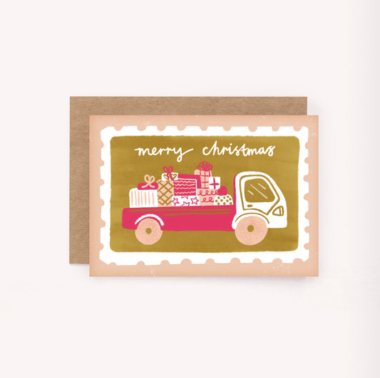 This playful Christmas card features a postage stamp set upon a peachy pink background, with gold and hot pink details. Hand-lettered across the top is "Merry Christmas"