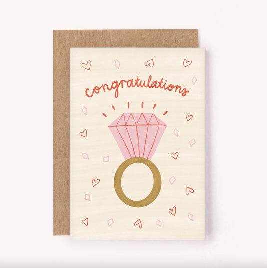 Send "Congratulations" to a newly engaged couple with this illustrated greeting card. Beige background is a pink engagement ring surrounded by mini hearts
