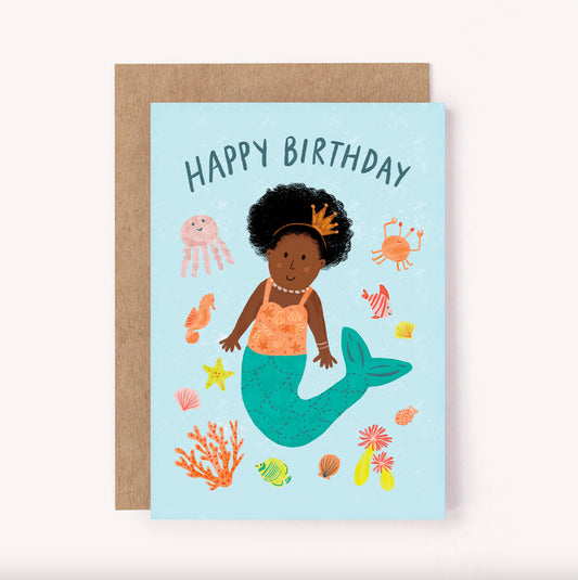 Illustrated "Happy Birthday" mermaid themed greeting card, perfect for a little one's special day. Features a beautiful mermaid surrounded by seashells, underwater plants and cute creatures on a bright blue background. She has an afro with a tiny gold crown headband, pearl necklace and a decorated orange top